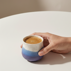 Hand holding a ceramic mug with a gradient design on a plain background