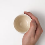 Hand holding a beige ceramic cup against a white background