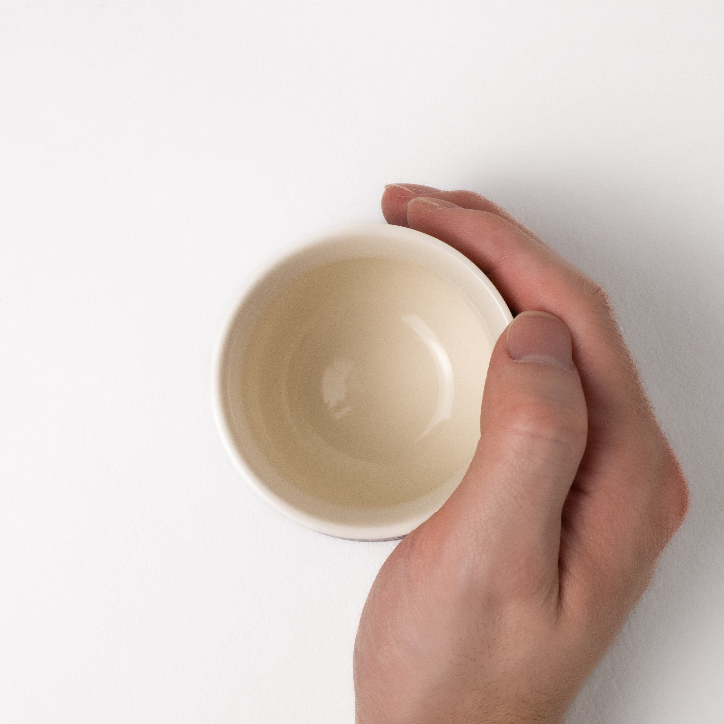 Hand holding a beige ceramic cup against a white background