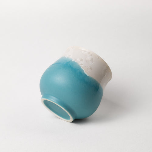 Ceramic tea cup with two-tone, white top, blue bottom design on a white background