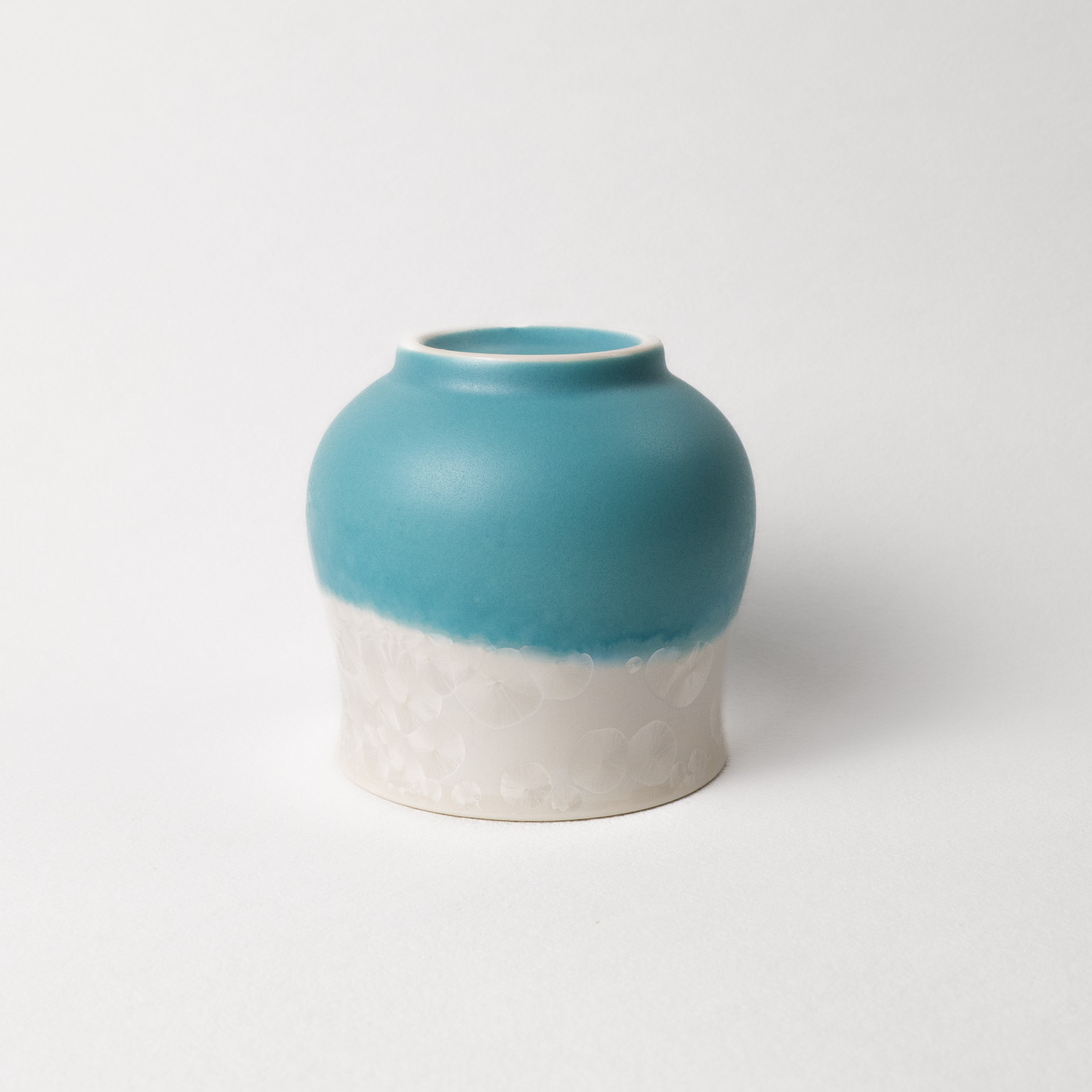 Ceramic cup with two-tone, white top, teal and light blue bottom design on a white background
