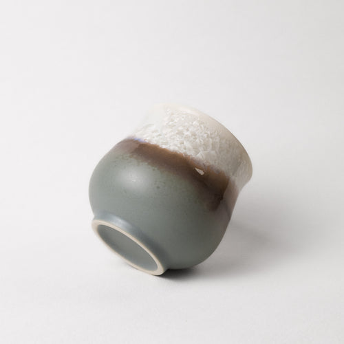 Ceramic cup with two-tone, white top, grey and brown bottom design on a white background
