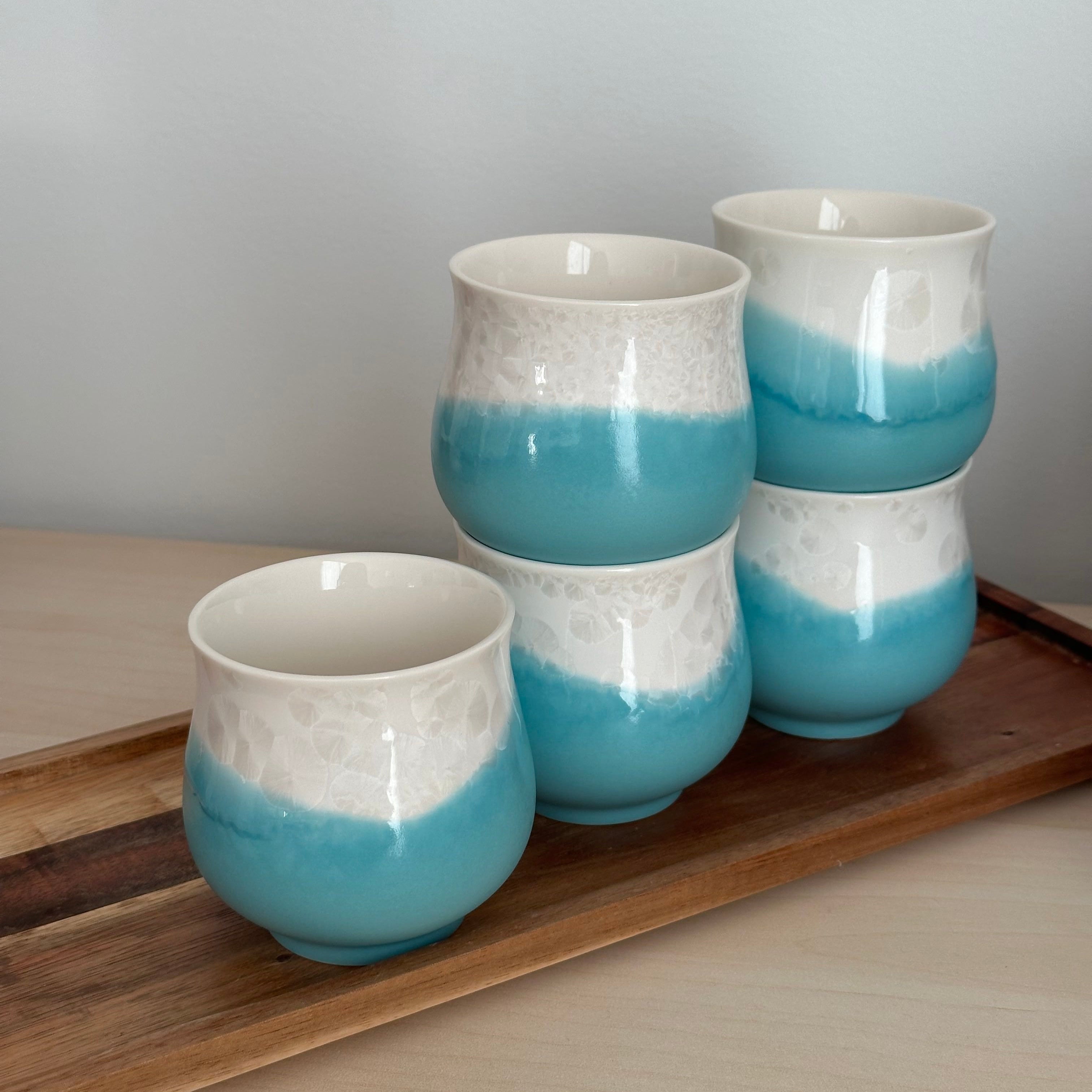 Set of four blue and white ceramic cups hanging on a wooden shelf against a light gray wall.