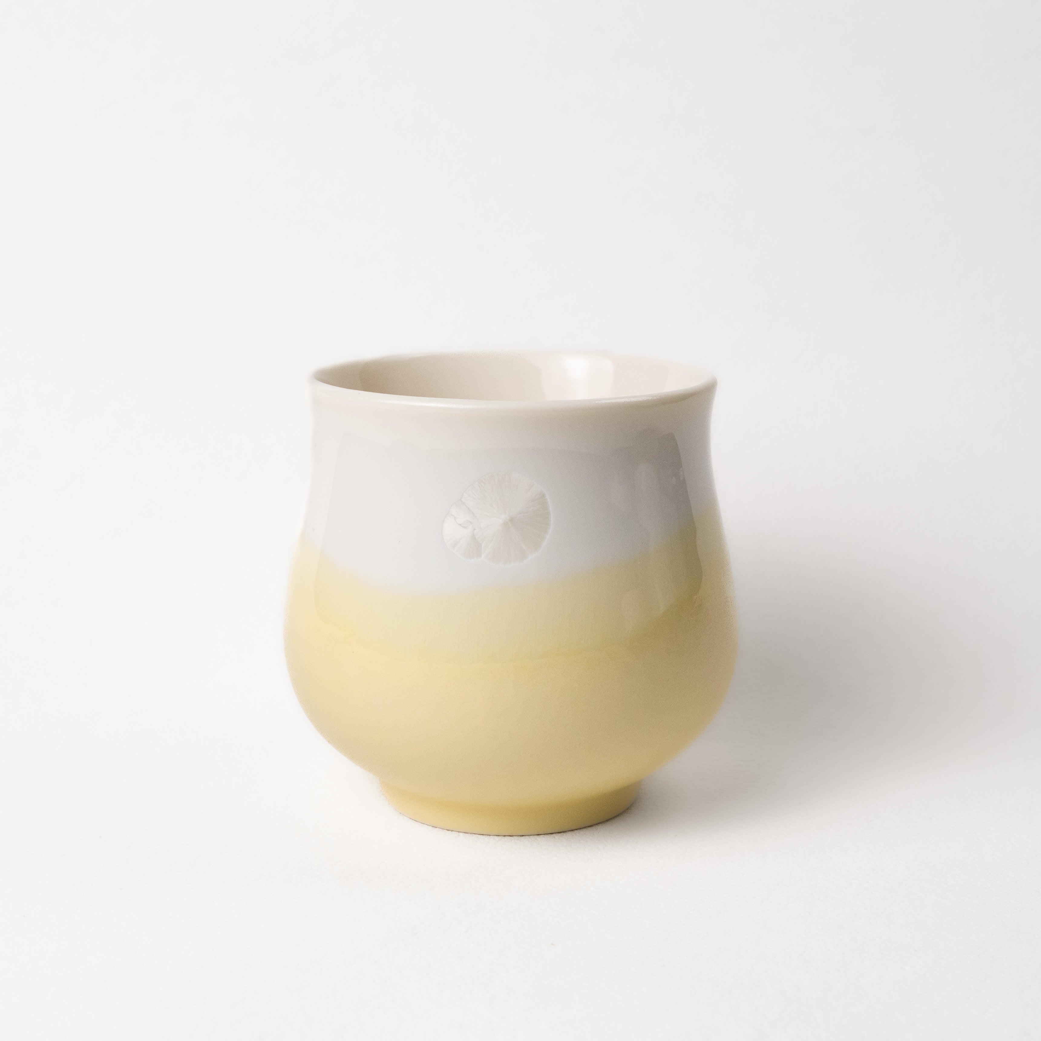 Ceramic cup with two-tone, white top, yellow bottom design on a white background