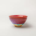 Ceramic tea cup with multicolored read and blue glaze on a white background