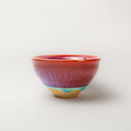 Ceramic tea cup with multicolored read and blue glaze on a white background