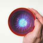 Hand holding a red ceramic tea cup with a colorful interior design on a white background