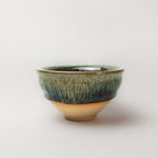 Ceramic tea cup with green and brown glaze on a white background