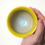 Hand holding a yellow ceramic tea cup with a textured interior