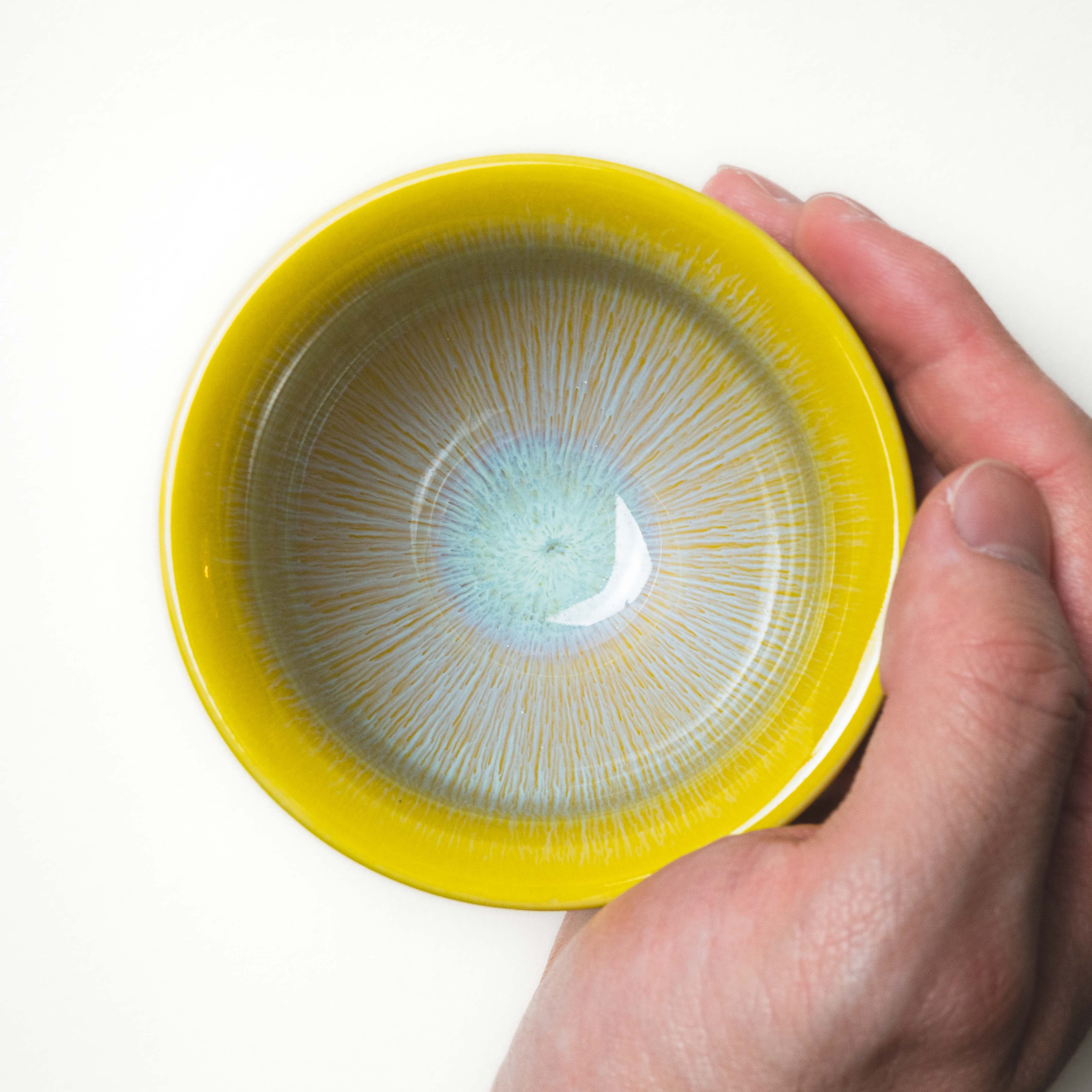 Hand holding a yellow ceramic tea cup with a textured interior