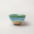 Ceramic tea cup with multicolored green and blue glaze on a white background