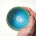 Hand holding a green ceramic tea cup with blue interior
