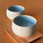 Two ceramic bowls with textured exterior and light blue interior on a wooden surface.