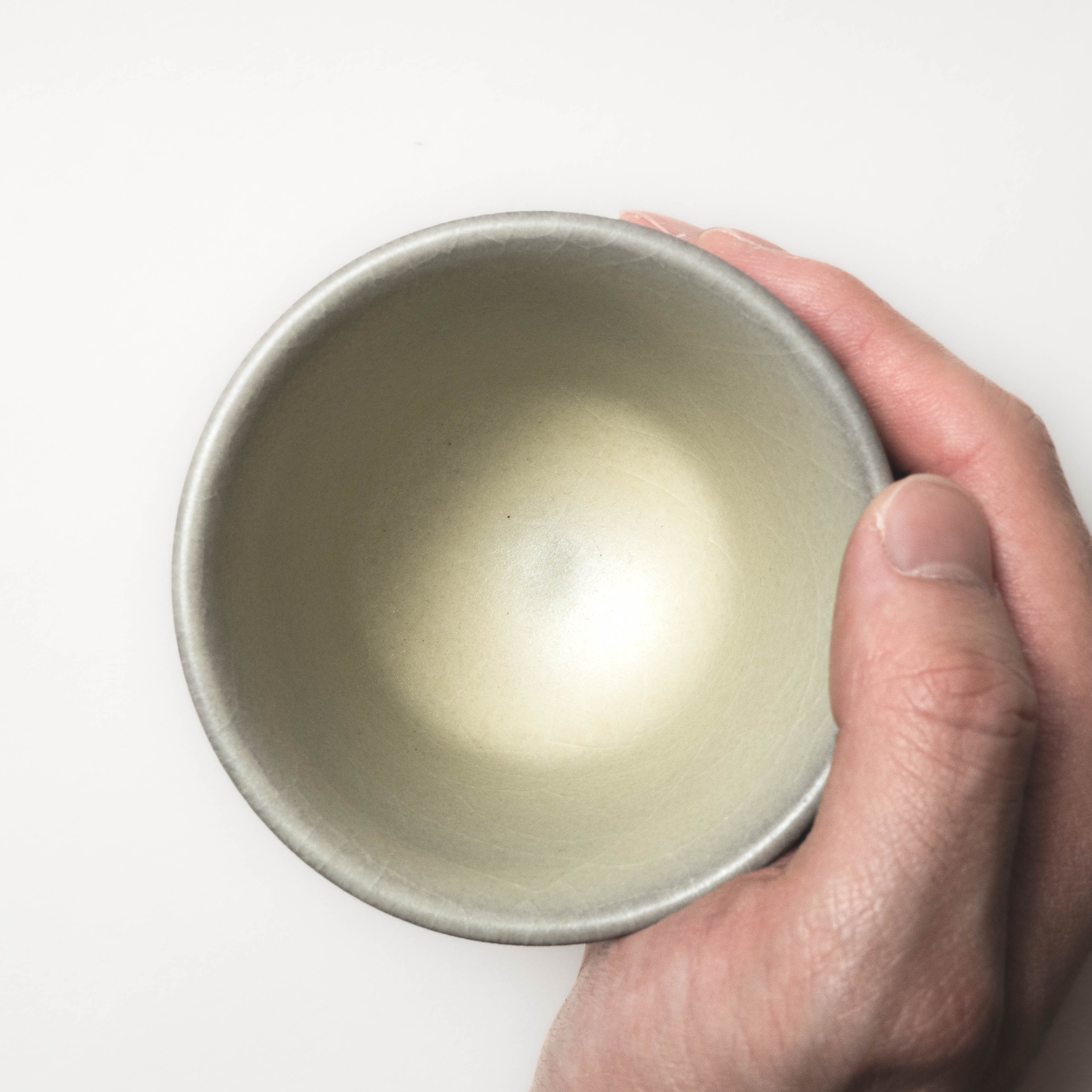 Hand holding a ceramic cup against a white background