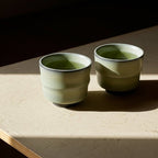 Two ceramic cups with green tea on a textured surface with a dark background