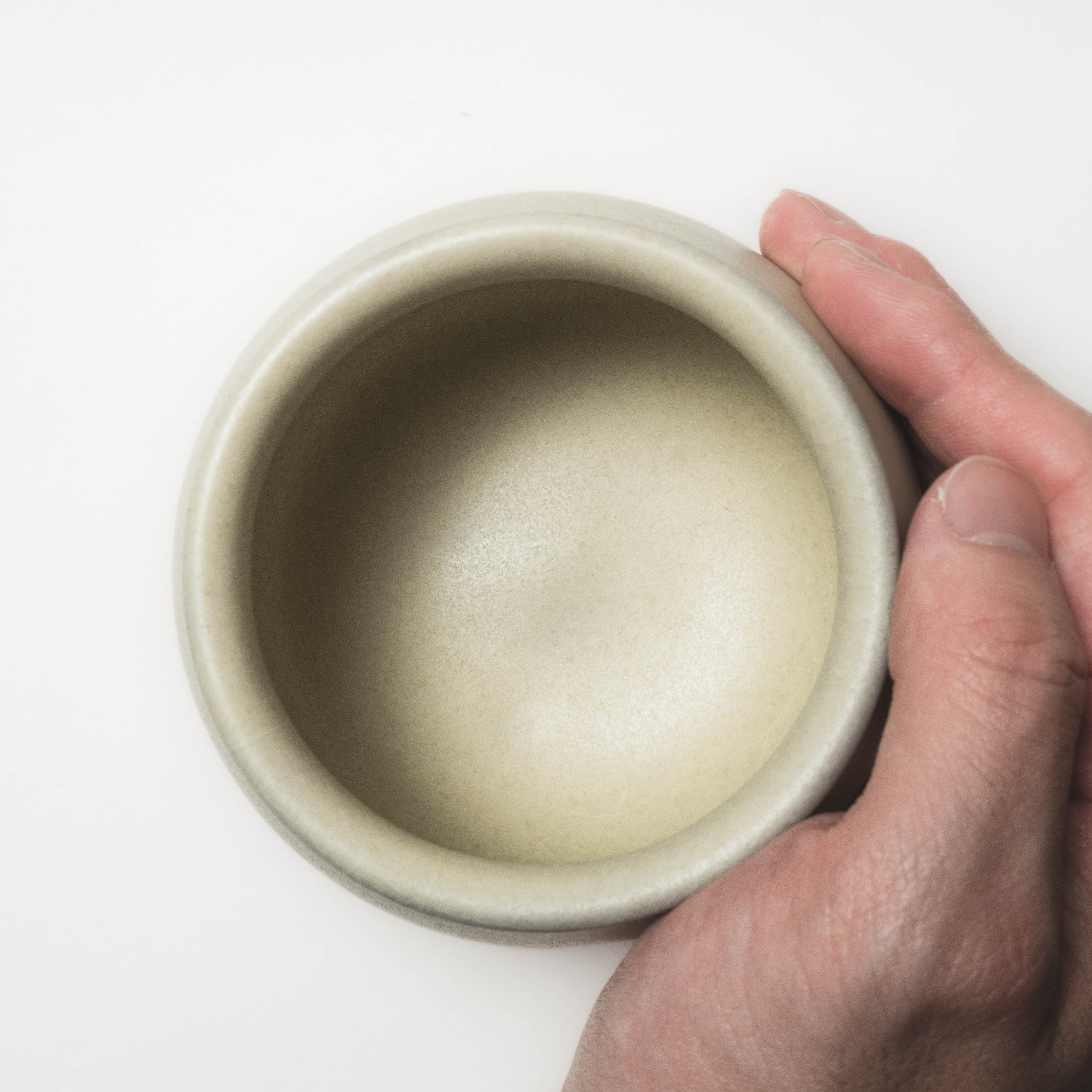 Hand holding a ceramic tea cup on a white background