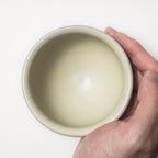 Hand holding a beige ceramic bowl against a white background